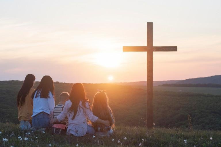 Familie sitzt vor einem Kreuz im Sonnenuntergang